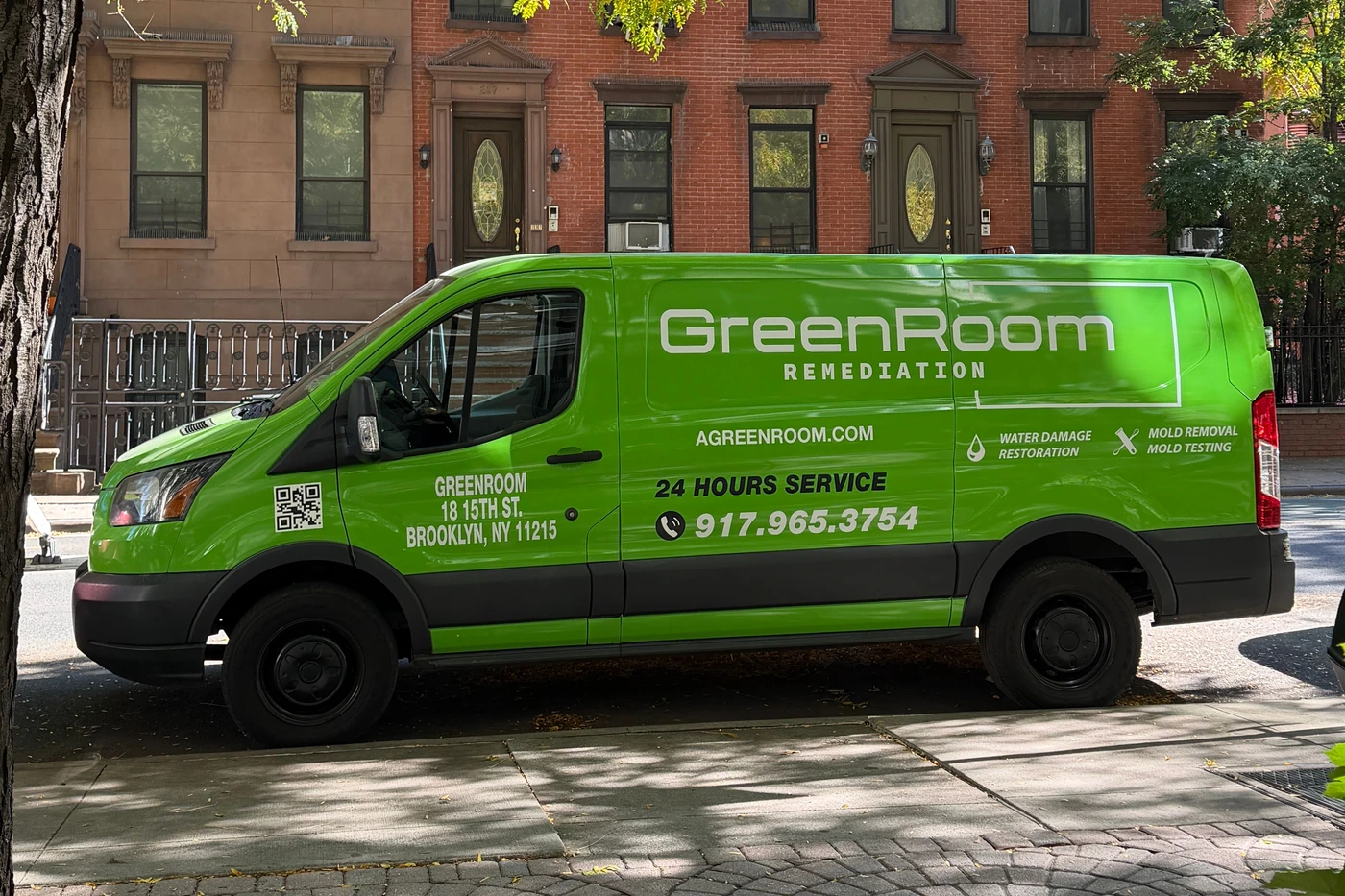 GreenRoom Remediation service van parked beneath a tree in front of brick townhouses