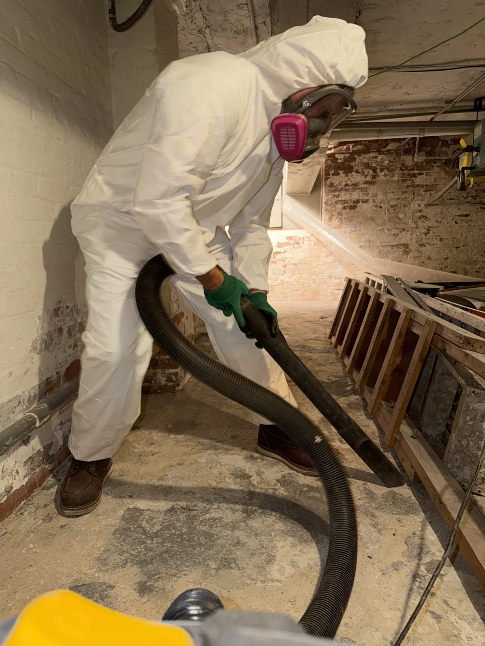 GreenRoom technician wearing protective coveralls, gloves and a respirator while vacuum-cleaning a basement floor