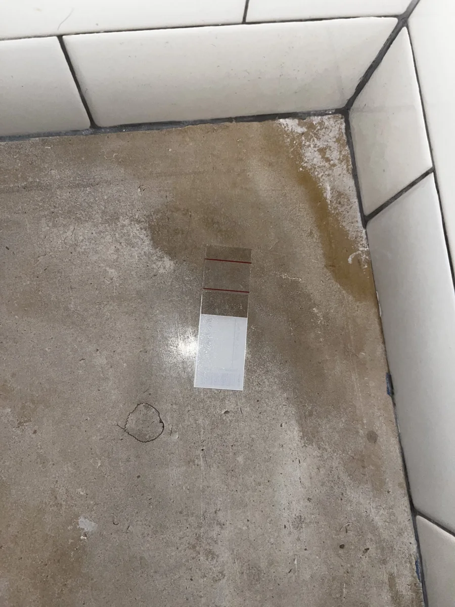 Transparent tape-lift sampling strip on a discolored surface beside tiles